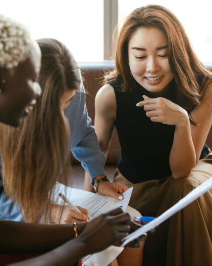 Three women in business attire leaning in over a written document