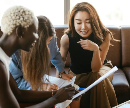 Three women in business attire leaning in over a written document