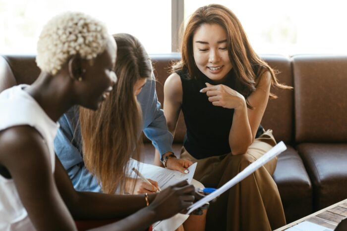 Three women in business attire leaning in over a written document