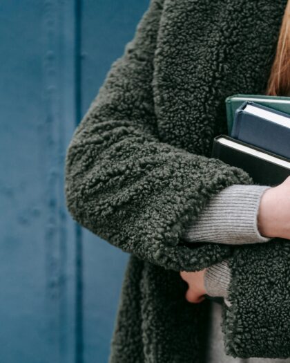 Zoomed in photo of person wearing green jacket with books held to chest