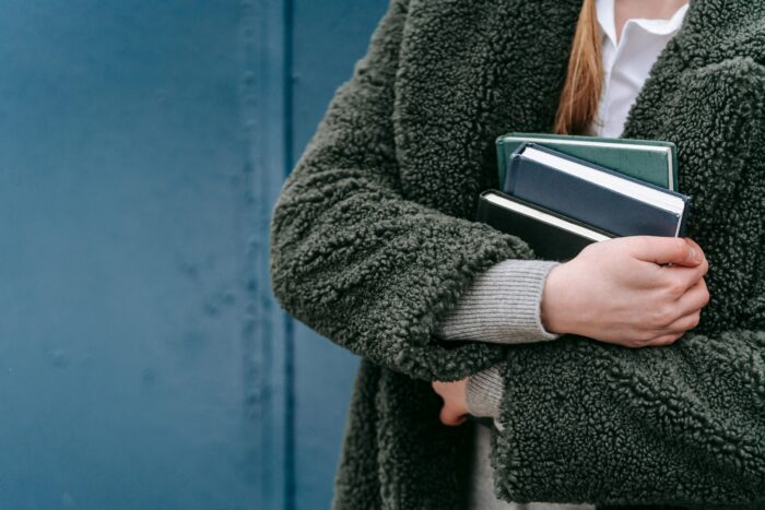 Zoomed in photo of person wearing green jacket with books held to chest