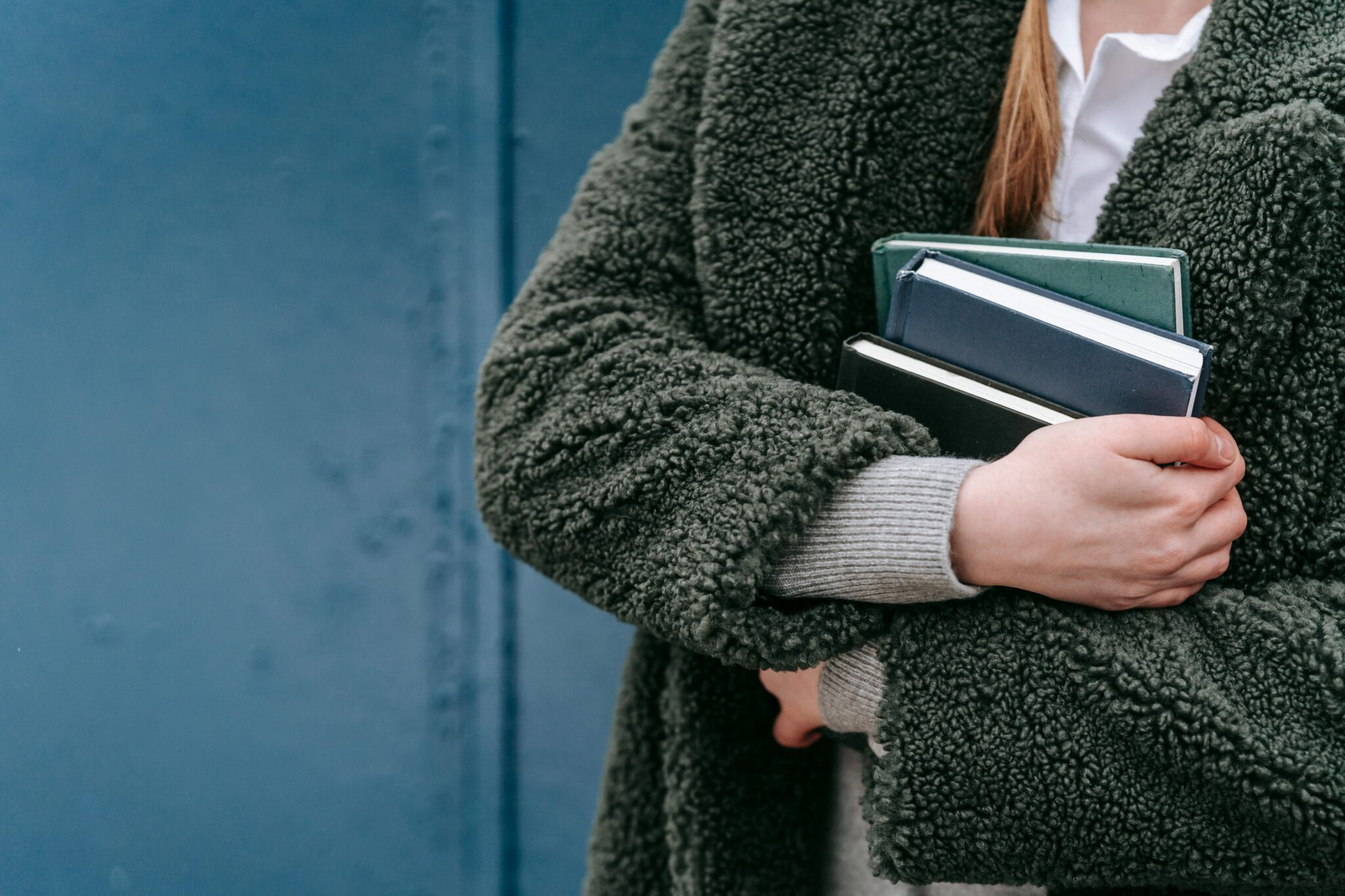 Zoomed in photo of person wearing green jacket with books held to chest