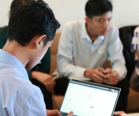 Over the shoulder of man in business attire looking at his laptop screen (blurred)