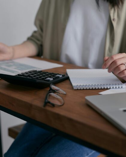 person sitting at desk with laptop, papers, and calculator