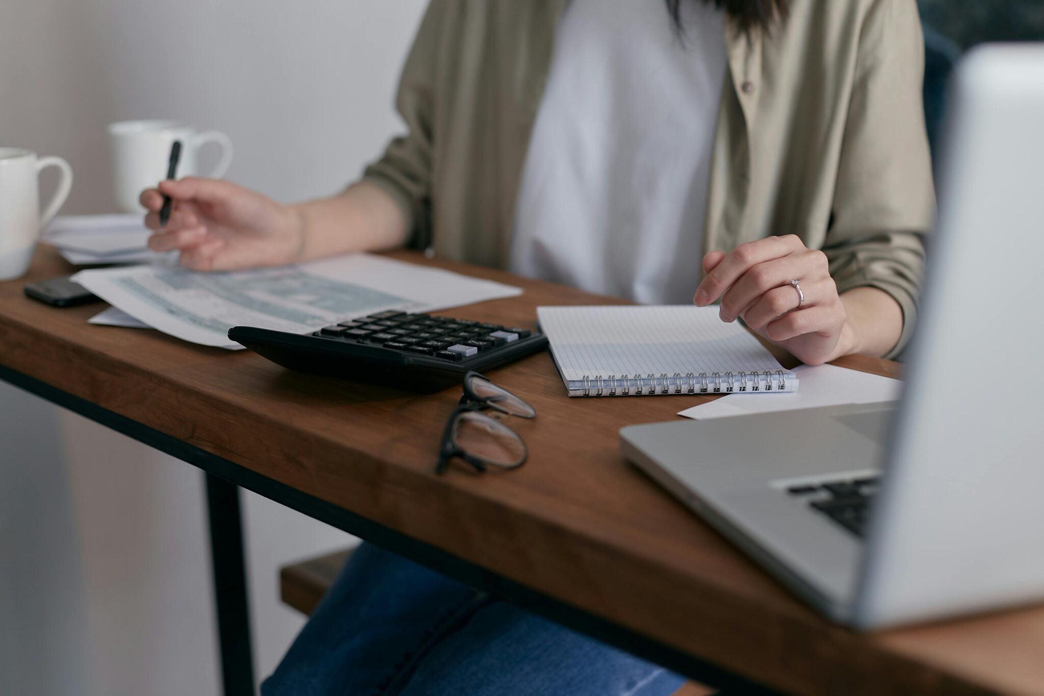 person sitting at desk with laptop, papers, and calculator