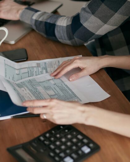 Hands holding documents on desk next to calculator