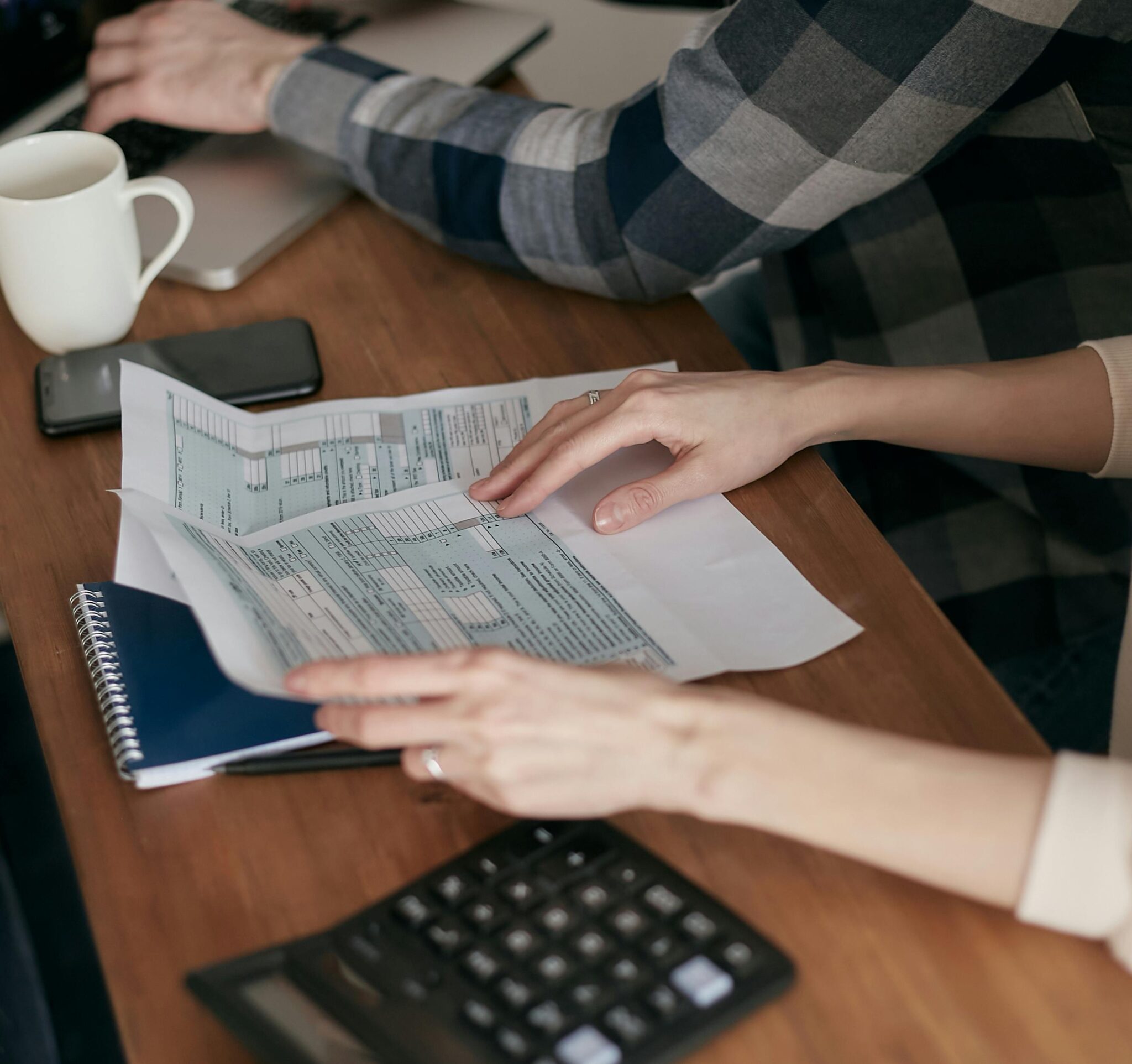 Hands holding documents on desk next to calculator