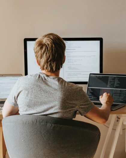 Person with back to camera facing three computer screens on desk.