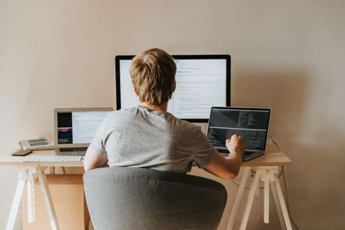 Person with back to camera facing three computer screens on desk.