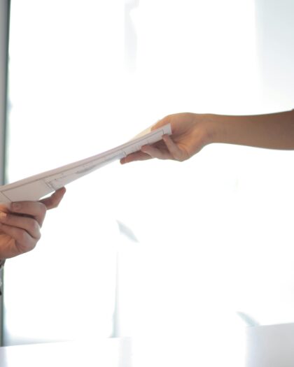 One arm with business casual sleeve handing other hand with business jacket sleeve a stack of papers