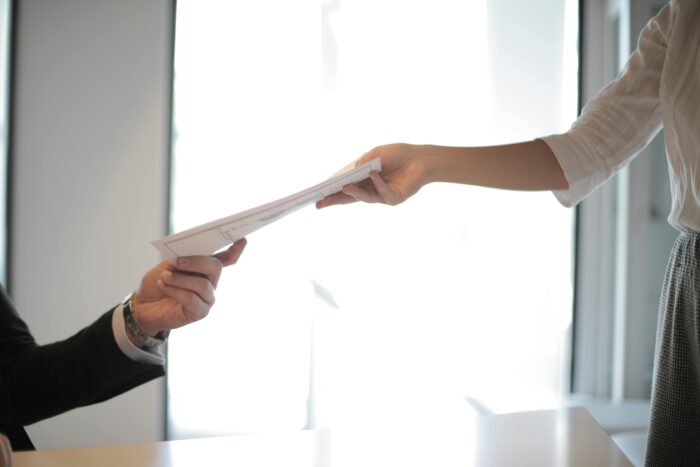 One arm with business casual sleeve handing other hand with business jacket sleeve a stack of papers