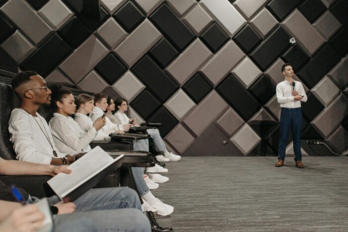 Group of students in business attire watching other student in business attire give lecture