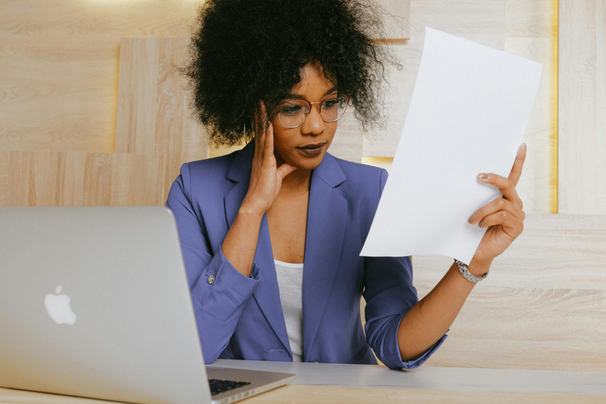 Woman sitting at desk with laptop, looking at paper in hand
