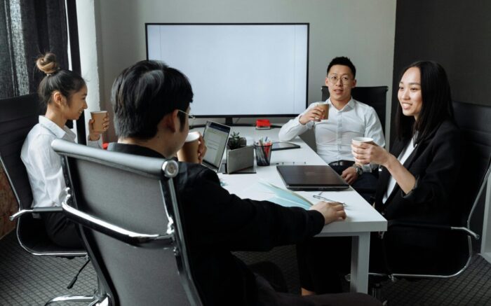 Four Asian business people around conference table with various papers and devices.