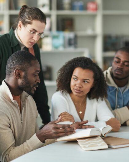 Group of students discussing a book at a library table.