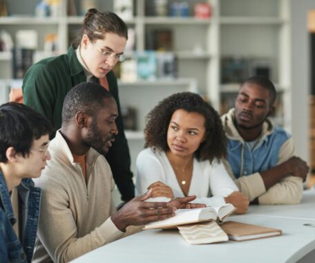 Group of students discussing a book at a library table.