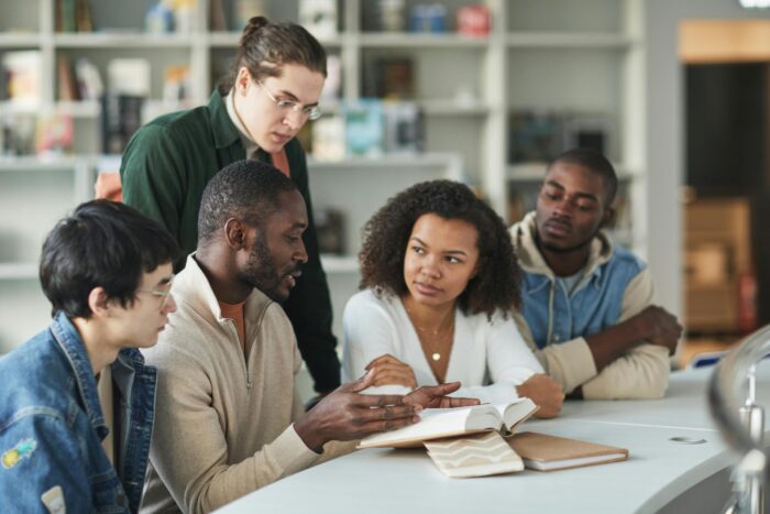 Group of students discussing a book at a library table.