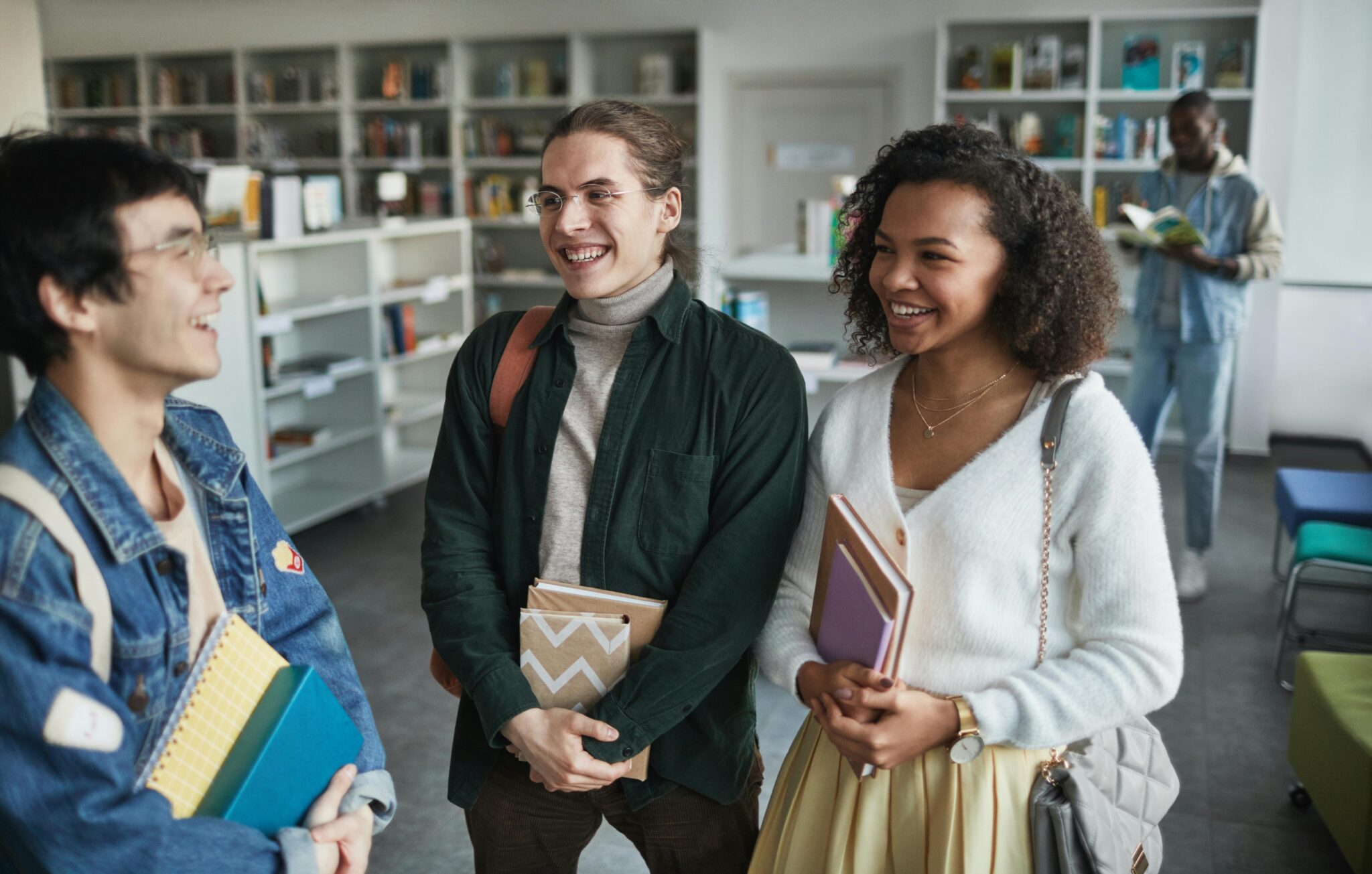 Two young girls and one young boy standing in a library, holding books and laughing together while discussion.