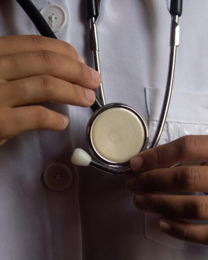 A young male doctor in white scrubs stands facing the camera, with a stethoscope visible around his neck
