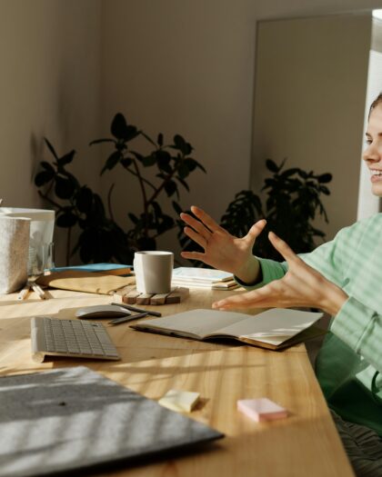 A young girl sitting at a study table with a MacBook, attending an online class while discussing her thoughts with her tutor.