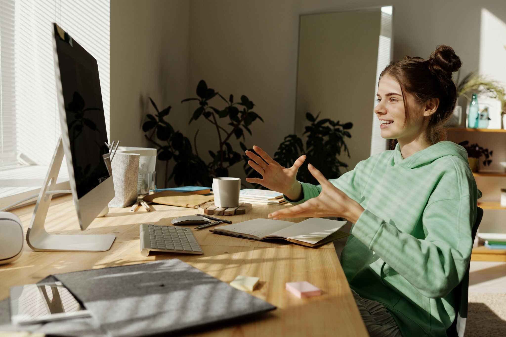 A young girl sitting at a study table with a MacBook, attending an online class while discussing her thoughts with her tutor.
