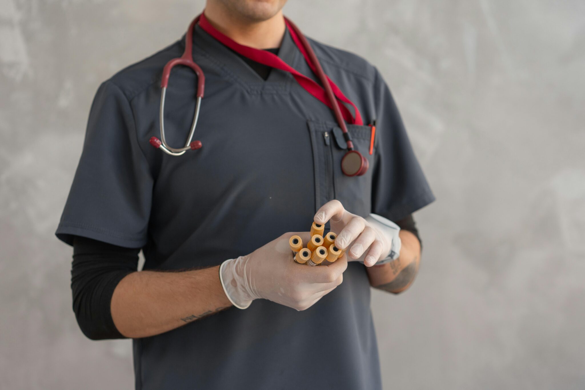 A male surgeon wearing a stethoscope and gloves holds injections on his hand