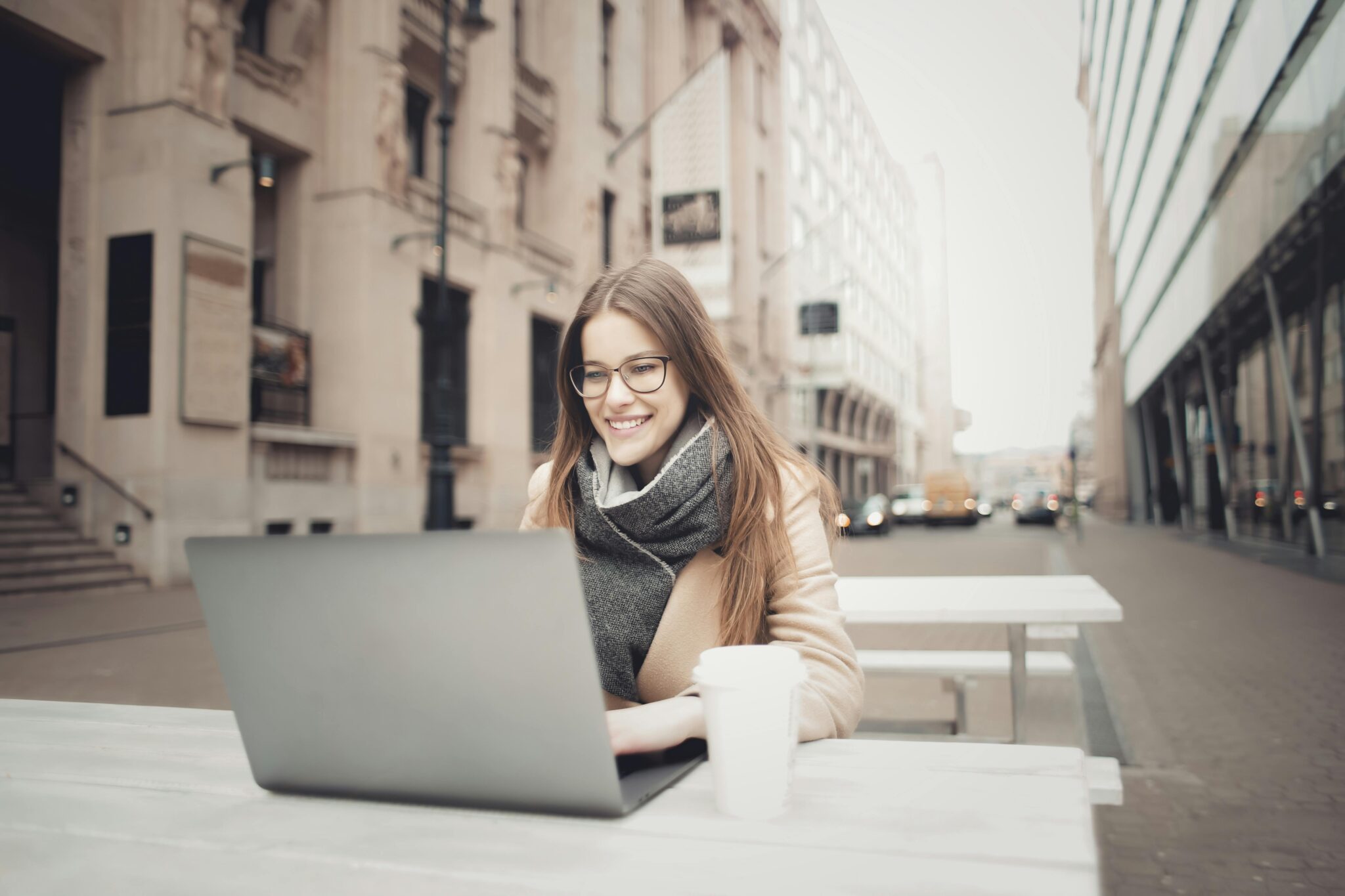 Woman sitting at outdoor table in Milan working on laptop next to a coffee