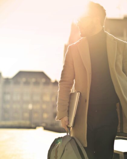 Man in trenchcoat with books walking in the sunlight