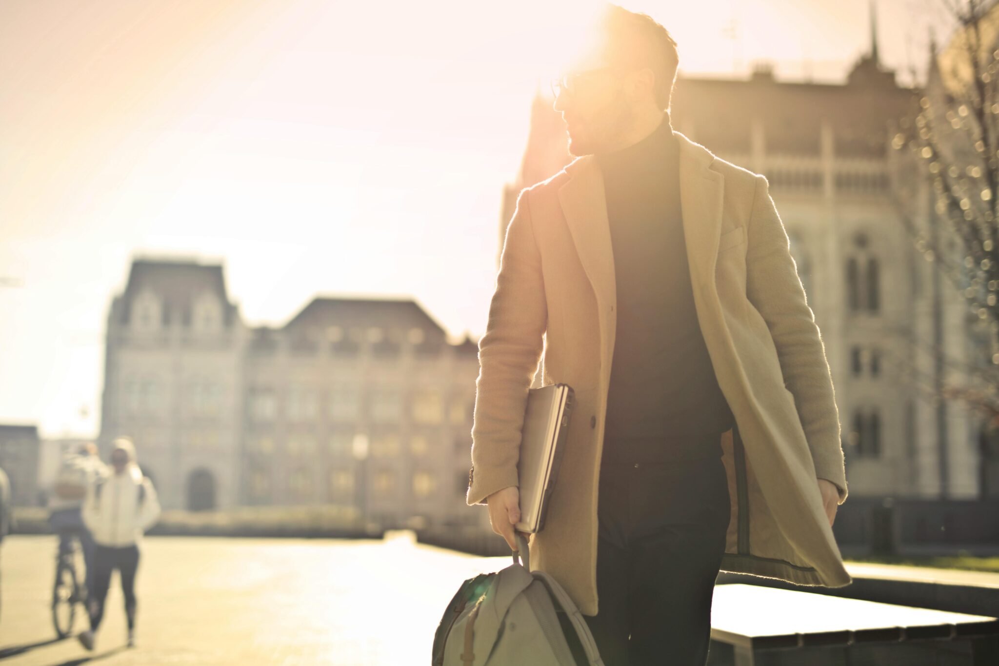 Man in trenchcoat with books walking in the sunlight