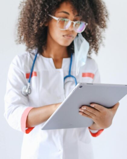 A young female doctor wearing a stethoscope reviews a patient's prescription on her tablet.