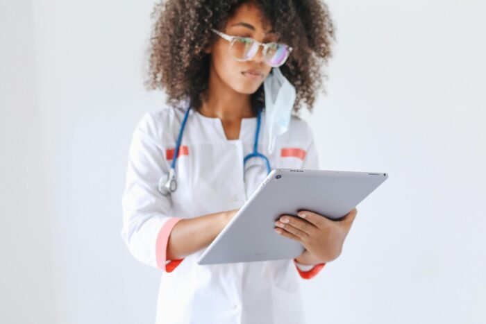 A young female doctor wearing a stethoscope reviews a patient's prescription on her tablet.