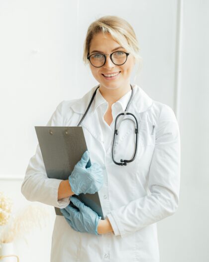 A photo of female Doctor holding a stethoscope and file looking towards the camera