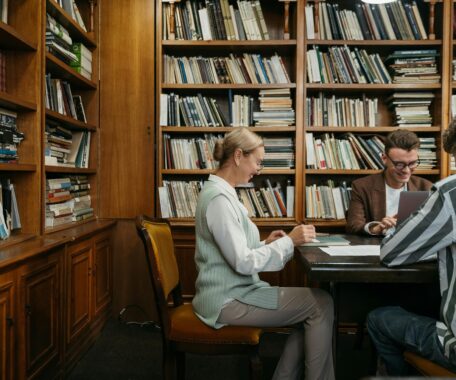 Two students and professor sitting at wooden library table