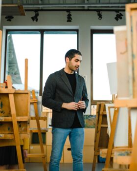 Man in Black Blazer Standing In a Room of Wooden Easels