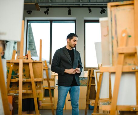 Man in Black Blazer Standing In a Room of Wooden Easels