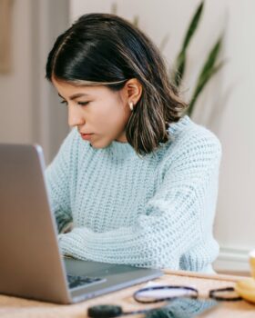 Hispanic female freelancer using laptop near coffee cup in apartment