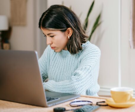 Hispanic female freelancer using laptop near coffee cup in apartment