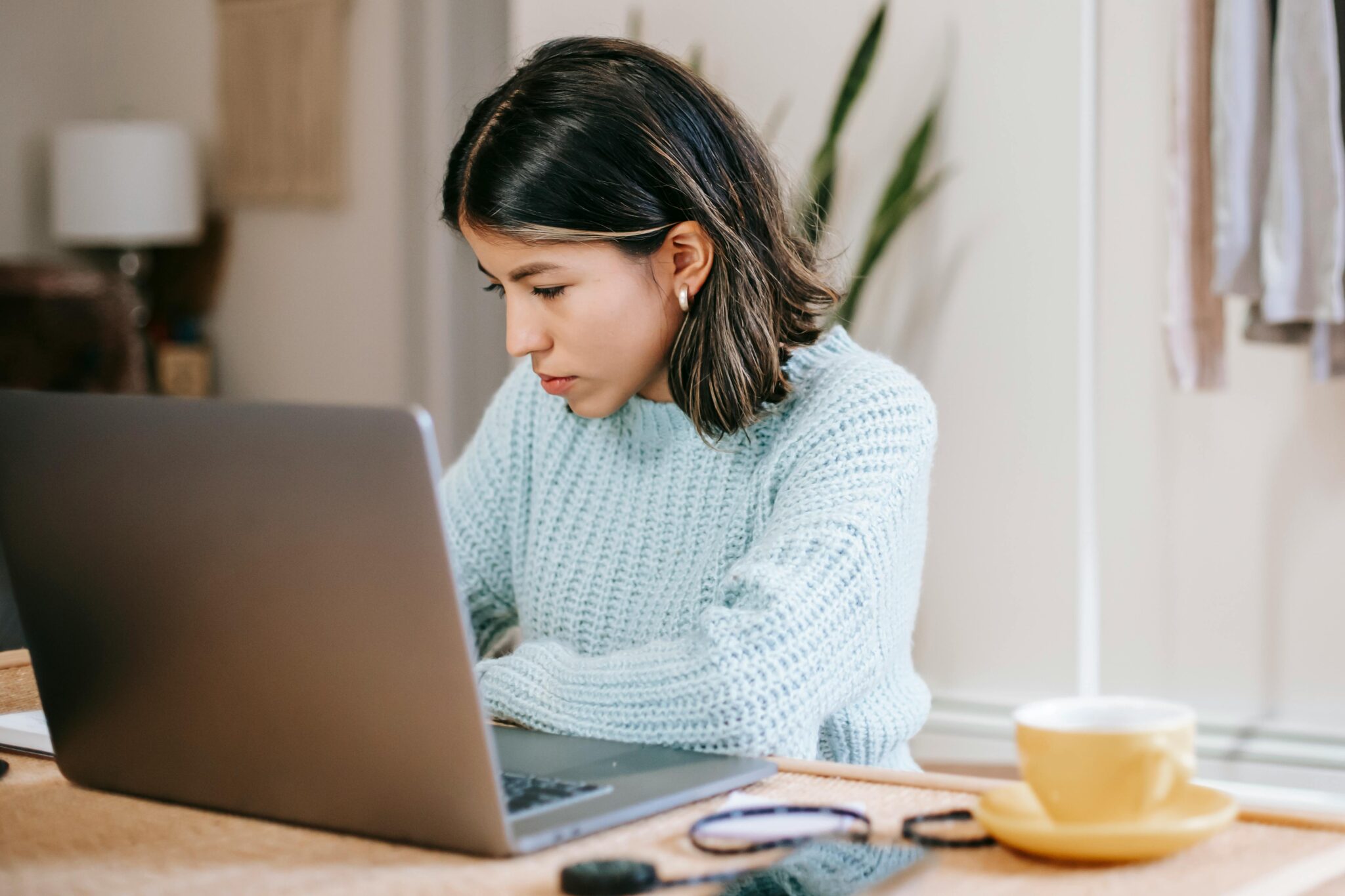 Hispanic female freelancer using laptop near coffee cup in apartment