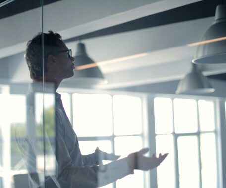 Man behind glass in business casual attire talking to someone off camera