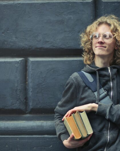 Young Man Leaning Against The Wall Holding A Books