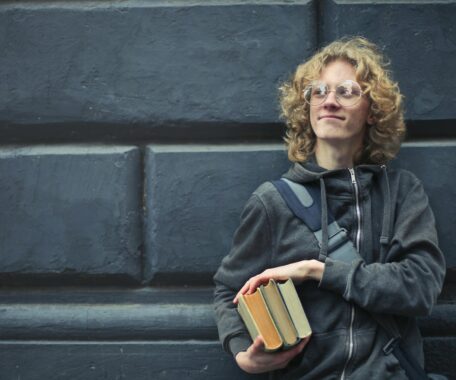 Young Man Leaning Against The Wall Holding A Books