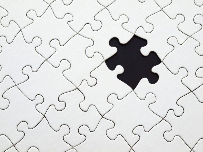 White puzzle pieces with a black space where there is a piece missing