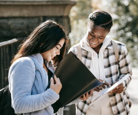 Cheerful multiracial students watching folders while studying on street