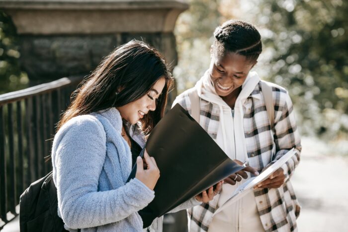 Cheerful multiracial students watching folders while studying on street