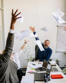 Colleagues in a meeting throw paper in the air while seated in a conference room