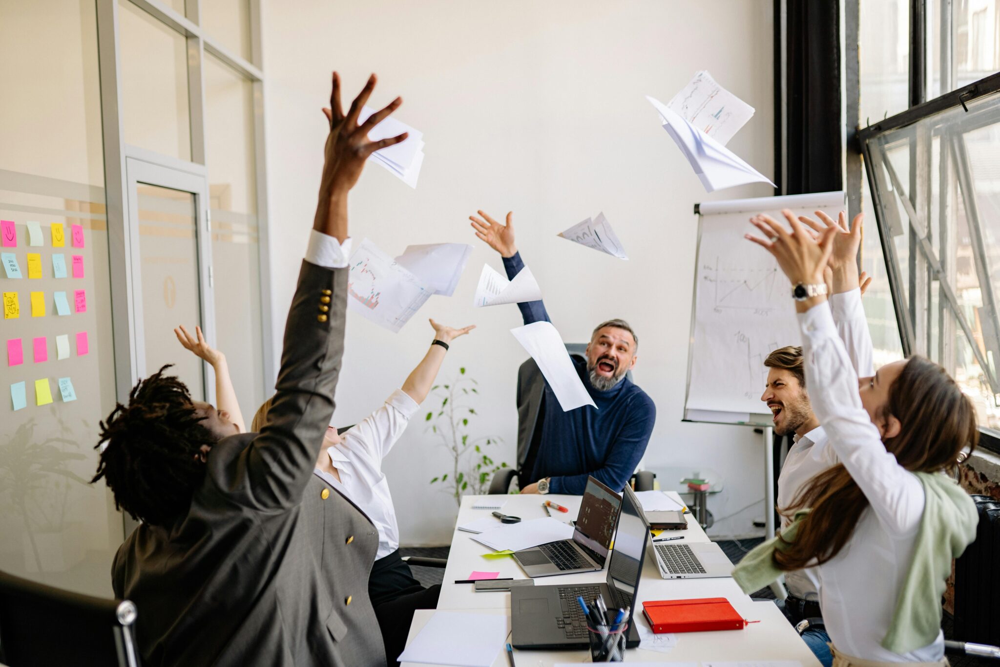 Colleagues in a meeting throw paper in the air while seated in a conference room