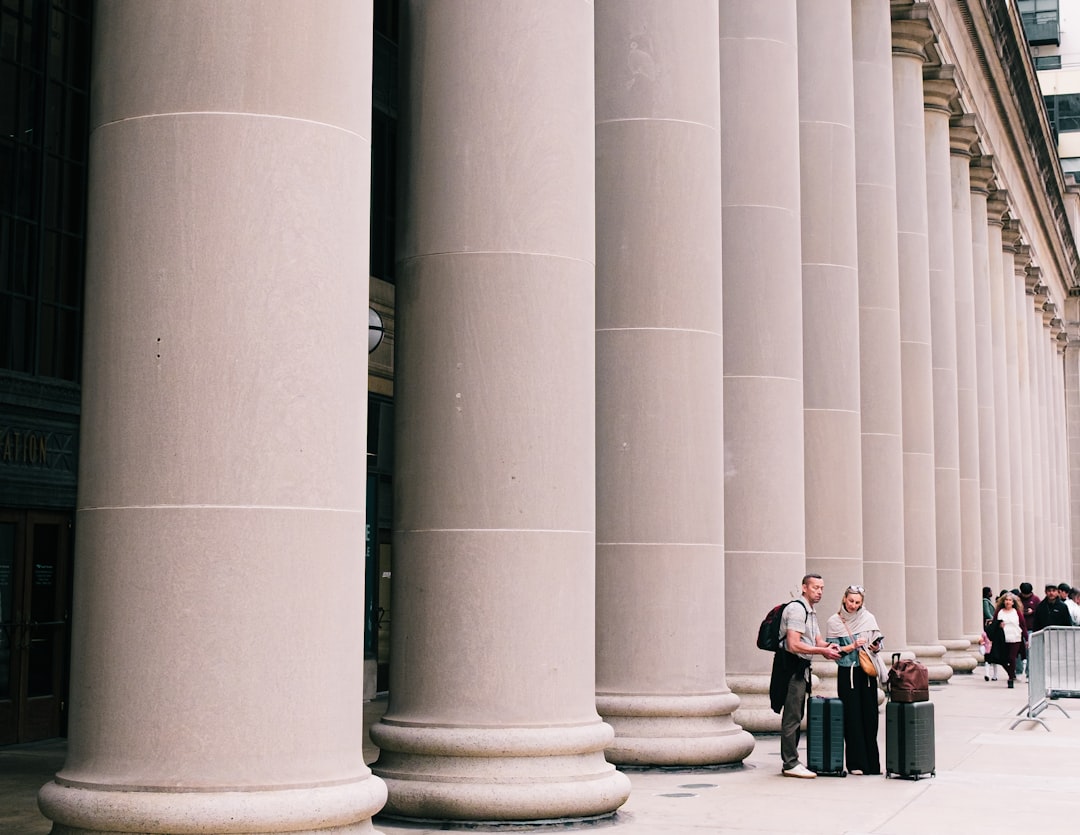 People walking past large stone columns outdoors