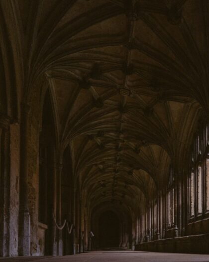 A dark, gothic hallway with arched ceilings and windows.